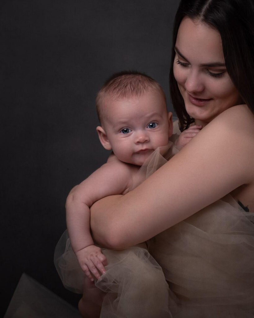 A mother holding her baby son as he looks into the camera with big blue eyes