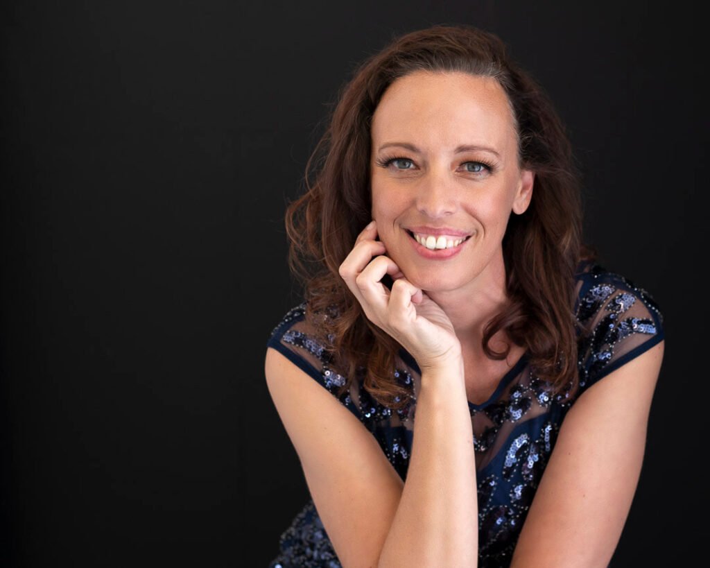 a photo of Denise Allen, the photographer, wearing a blue dress and posing on a black background.