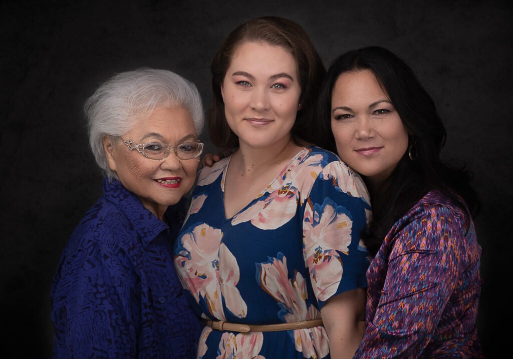 Three generations of women posing with the youngest in between her mother and grandmother.